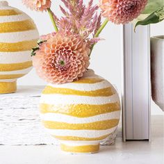 two vases with flowers in them sitting on a table next to an open book