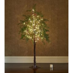 a lighted christmas tree on a wooden table in front of a wall with a brown background