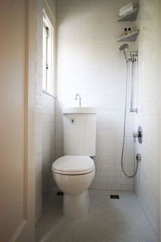 a white toilet sitting inside of a bathroom next to a shower head mounted on a wall