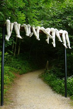 sculptures hanging from poles in the middle of a dirt path surrounded by trees and greenery