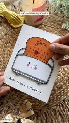 someone holding up a birthday card with a toaster on it and candles in the background