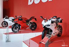 three motorcycles are on display in front of a red wall and sign that says duc