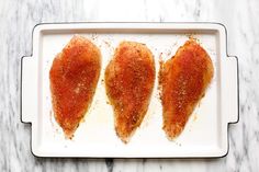 three pieces of chicken on a white plate with seasoning sprinkled over them