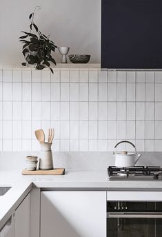 a kitchen with white tiles and wooden utensils on the counter top, next to a potted plant