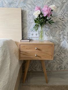 a nightstand with flowers on it next to a wallpapered bed and night stand