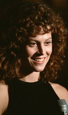 a woman with curly hair is smiling and holding a microphone in her hand while wearing a black tank top