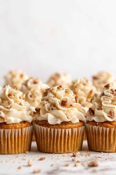 several cupcakes with white frosting and walnuts on top are lined up