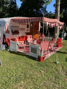 a red and white food truck parked on top of a grass covered field next to trees