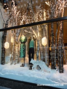 a window display with trees and lights in the snow, including a woman standing next to a dog