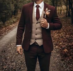 a man in a suit and tie standing on a dirt road with trees behind him