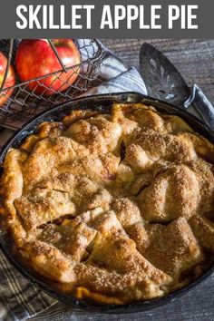 an apple pie in a cast iron skillet on a table next to some apples