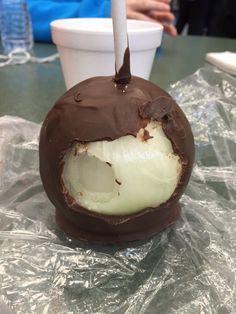 a chocolate covered dessert sitting on top of a plastic wrapper next to a cup