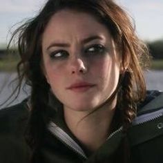 a woman with braids on her hair looking at the camera while standing in front of water