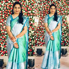 a woman in a blue and green sari standing next to a flower covered wall