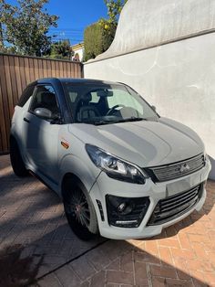 a silver car is parked in front of a wall and some bushes on the sidewalk