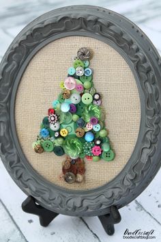 a small christmas tree made out of buttons in a frame on a table with a cat