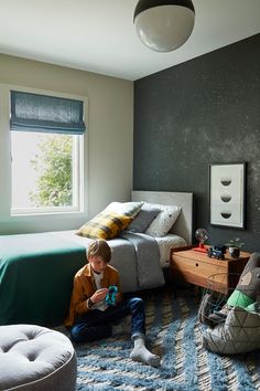 a young boy sitting on the floor playing with his toys in a bedroom that has space themed walls