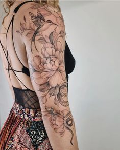 a woman's back with flowers and birds on her arm, in front of a white wall