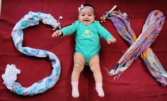 a baby laying on top of a red blanket next to various scarves and headbands