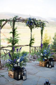 an outdoor ceremony setup with blue flowers and greenery on the arbor, along with lanterns