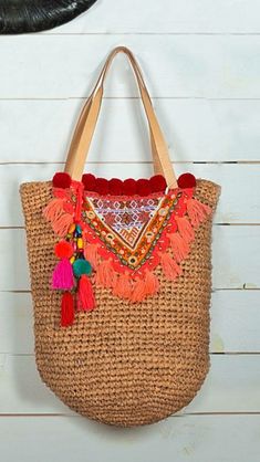 a straw bag hanging on the wall with tassels and pom poms