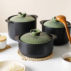 three black pots with wooden spoons sitting on a white counter top next to plates and bowls