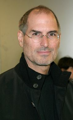 a man with glasses and a black jacket is looking at the camera while standing in a room