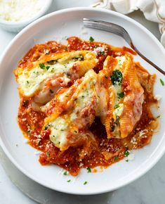 a white plate topped with lasagna covered in sauce and cheese next to a bowl of rice