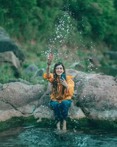 a woman is standing in the water with her hands up and splashing water on her face