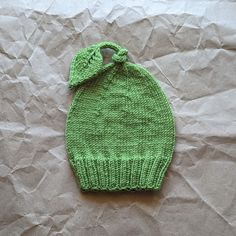 a green knitted beanie with a bow on the top sitting on crumpled paper