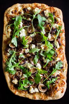 a pizza topped with mushrooms and greens on top of a black countertop next to a knife