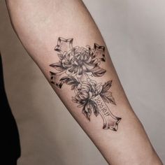 a woman's arm with a cross and flowers tattooed on the left inner arm