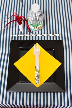 a black plate topped with a yellow napkin and fork