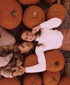 two women standing in front of pumpkins on the ground with their arms around each other