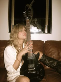 a woman sitting on top of a brown couch holding a black guitar in her hands