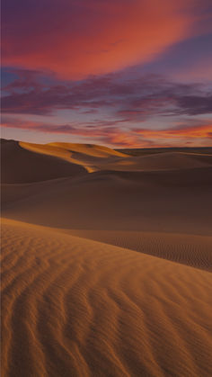 an orange and purple sunset in the desert with sand dunes on either side, as seen from above