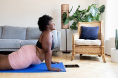 a woman doing yoga on a blue mat in front of a couch and potted plant