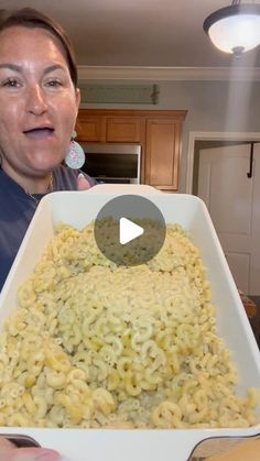 a woman holding a large white dish filled with macaroni and cheese