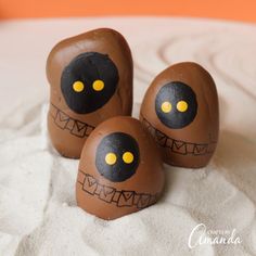 three chocolate eggs with painted faces on them sitting in the middle of some white sand