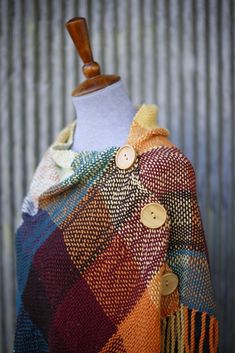 a mannequin wearing a multicolored plaid ponchy with wooden buttons