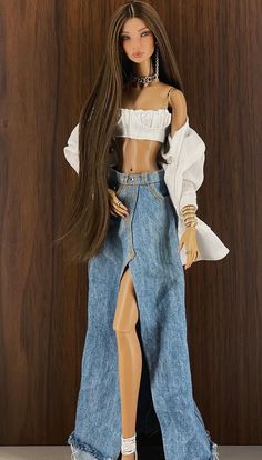 a doll with long brown hair wearing a white top and blue jean skirt, standing on a wooden surface