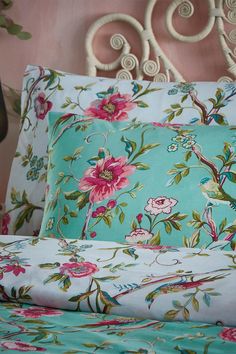 a bed topped with lots of pillows next to a headboard covered in pink and green flowers