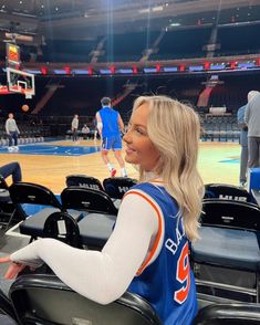 a woman sitting in a chair at a basketball game wearing a blue and white jersey