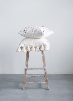 a white pillow sitting on top of a wooden stool with pom - poms