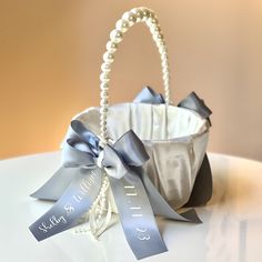 a white basket with silver ribbons and pearls on the handle is sitting on a table