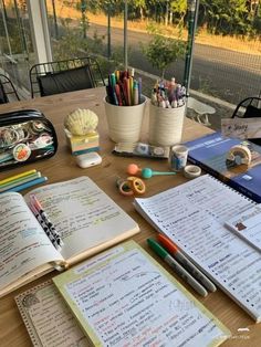 an open notebook sitting on top of a wooden table next to pens and pencils