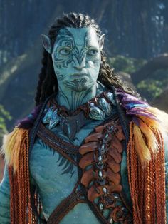 a man with dreadlocks and blue skin wearing an elaborate costume in front of mountains