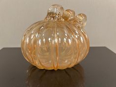 a glass pumpkin shaped object sitting on top of a black table next to a white wall