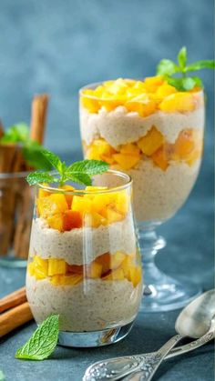 two glasses filled with fruit and oatmeal on top of a blue table