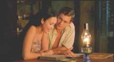 a man and woman sitting at a table in front of a book with a candle